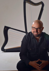 Eduardo Betancourt sitting and smiling in front of two large diatonic harps.