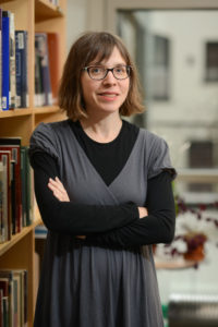 Barb Elam, Associate Director of Visual Media Resources and Study Collection Librarian for the Bard Graduate Center, stands smiling with crossed arms in front of a bookshelf.