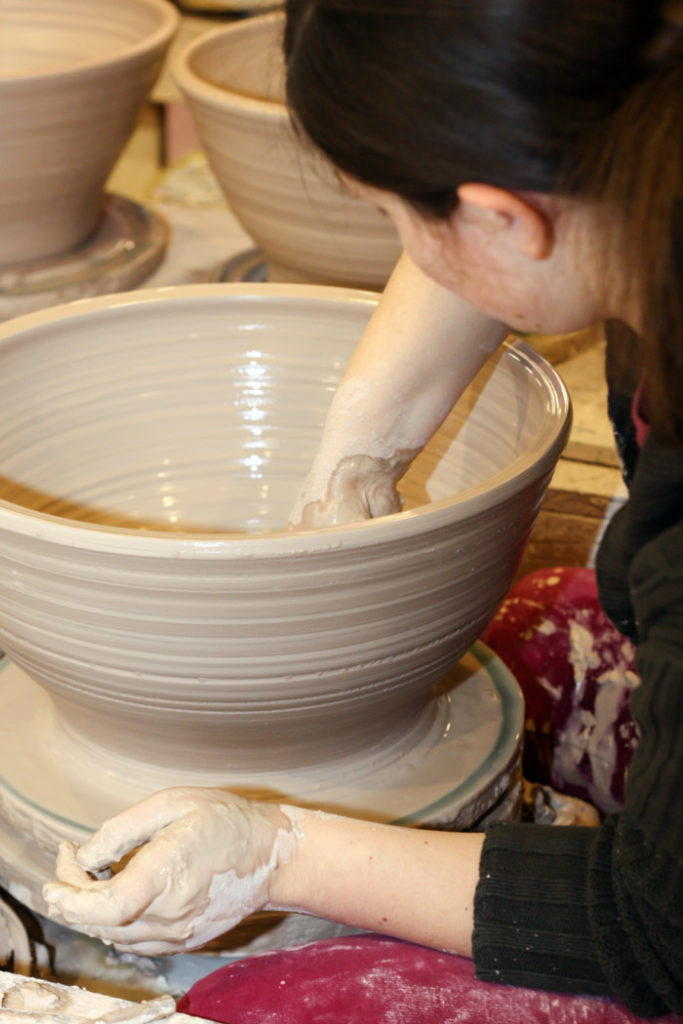 Closeup of Pottery Studio Artist Tessa Peterzak as she shapes a large clay vessel.