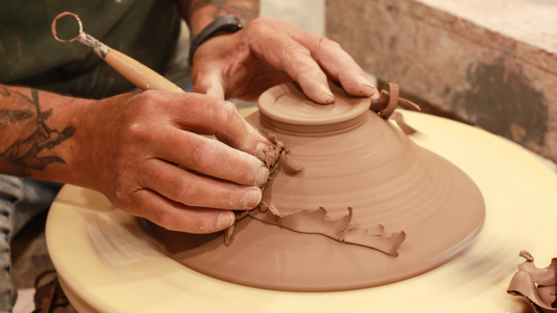 Closeup of a pair of hands carving into a clay bowl, spinning on the potters wheel.