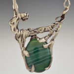 A golden necklace holding a smooth green stone by Harriet Forman Barrett.