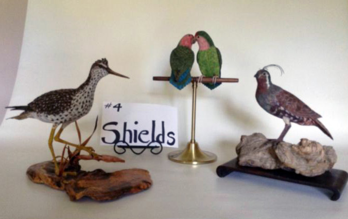 Carved birds by David & Barbara Shields. From left to right: a spotted bird with long legs on a wood platform, two birds together on a little stand, and a brown bird on a piece of wood.