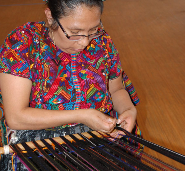 A woman carefully weaves on a loom.