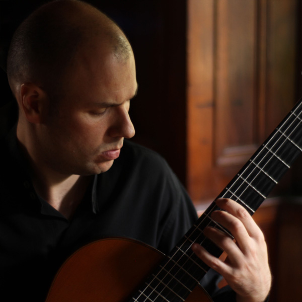 A closeup of Carlos Pavan looking downward, playing a guitar.