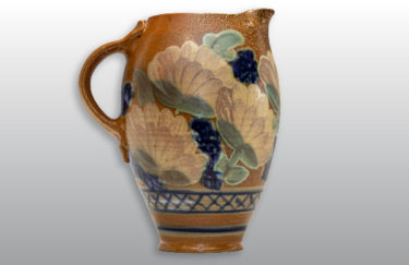 A tall tan ceramic pitcher with a floral pattern by Terry Plasket.