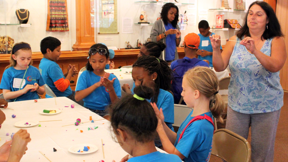 Children and a teacher in a student group create beads by rolling clay between their hands.