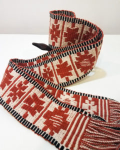 A woven belt with striking red block designs and a white and black striped border on the top and bottom.