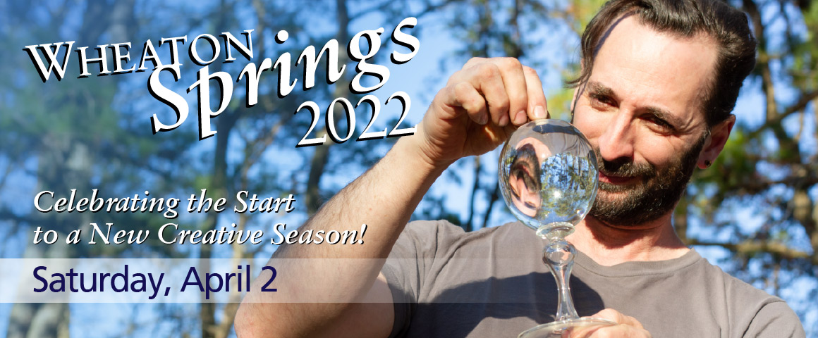 Glass artist Alex Rosenburg looks through an optical glass instrument with his reflection showing through to the other side of the glass. The trees and sky are blurred in the background. White text overlays that reads: “Wheaton Springs 2022: Celebrate the Start to a New Creative Season. Saturday, April 2”.