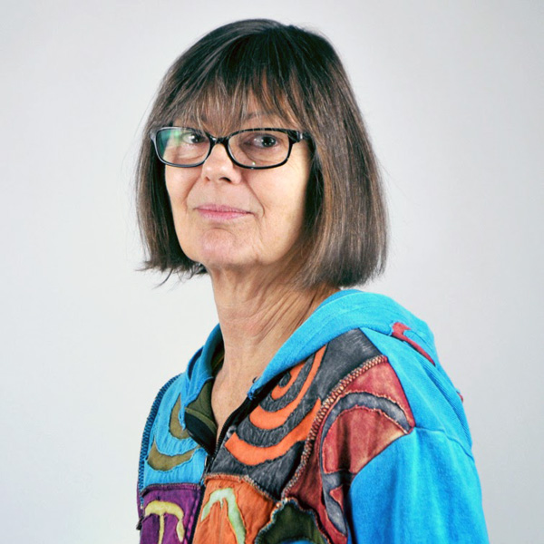 Deb DiMarco poses for a headshot with black glasses and short brown hair.