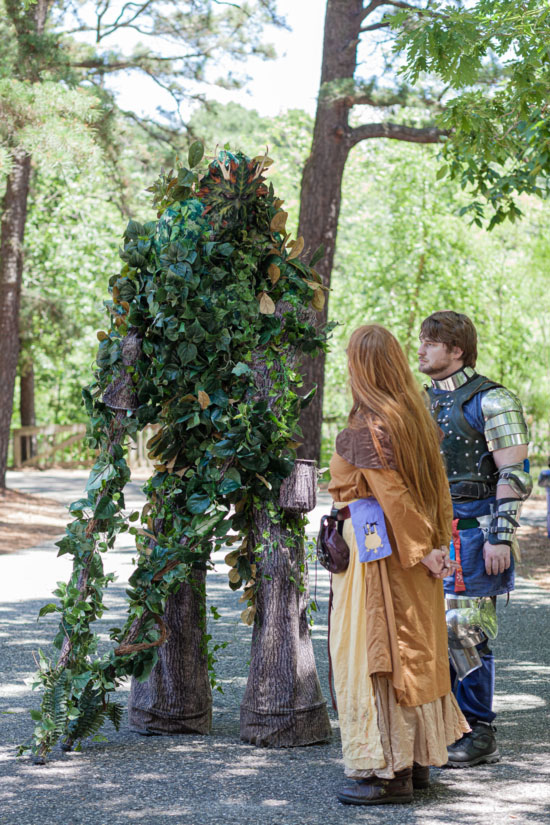 Fantasy Faire 2019 attendees dressed in fantasy costumes stand next to a life-like tree creature outdoors.