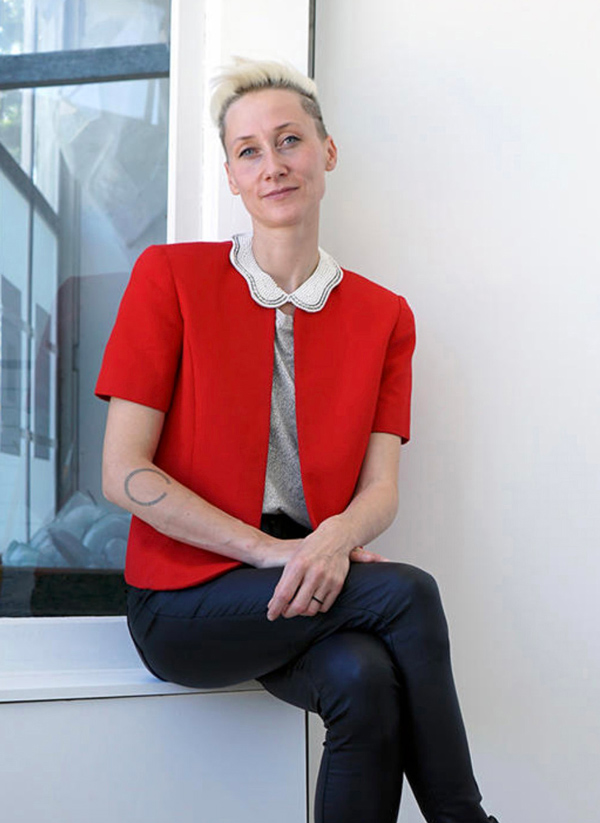 Headshot of Anna Mlasowsky seated on a window ledge. Anna wears a red blazer and white collared top and black pants.
