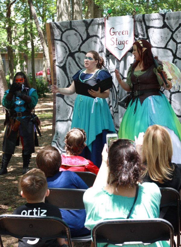 Fantasy Faire 2019 actors perform on the green stage in front of a watching audience outdoors.