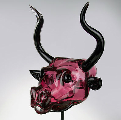 A glass sculpture, Rhyton Pink, of a dark red bull with black horns hangs alone in the center of a white background.