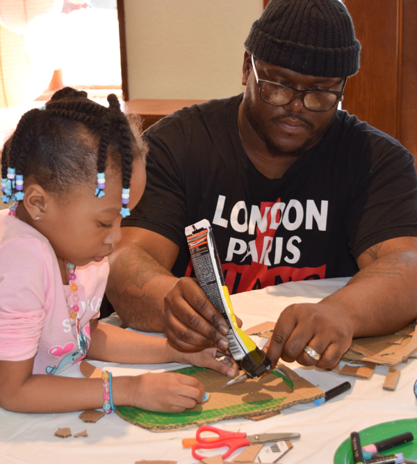 A parent helps his daughter to complete a Family Arts Workshop craft project.