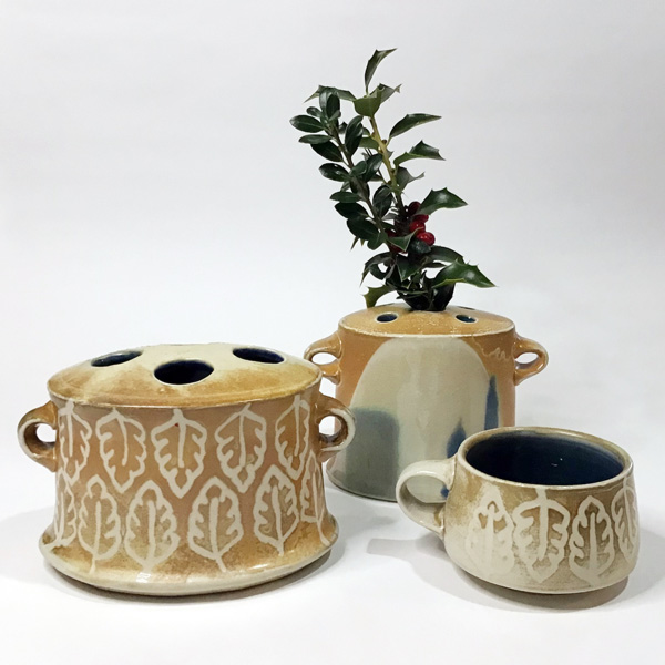 Three item from the Holiday Studio Sale. All of them are light brown with a white fade and two items in the front with white leaves around them. The one on the right is a mug and the other two appear to be plant holders as the one in the back has a plant in the center of it. There are three holes on the top of each plant holder.