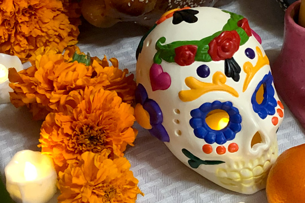 A close-up of an altar made by the HalloWheaton: Remembering Your Ancestors Celebration Special Program Tecuanis dance group with a Day-of-The-Dead multicolored skull on top of a grey table cloth. Around the skull are orange flowers and candles.