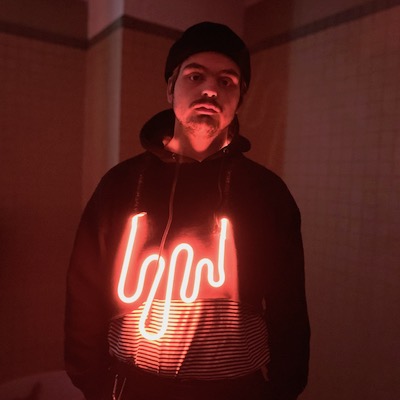 Jacob Willcox in a blackhoodie wearing one of his glass neon signs.