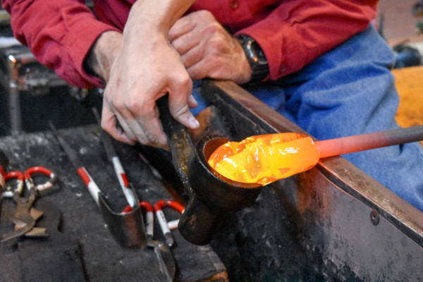 a close-up of hot glass being shaped by a metal cup-like tool.