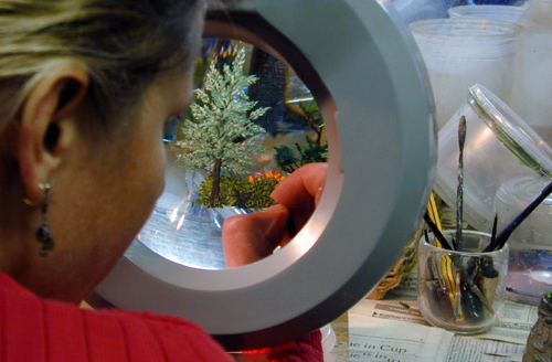 An over-the-shoulder shot of "Paperweight Fest 2023" demonstrating artist, Alison Ruzsa, is painting intricate glass trees.