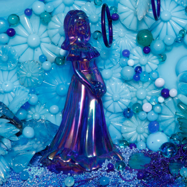 A close-up of the detail on the Alchemy of Adornment exhibit artist amber Cowan's glass sculpture is of a blue "bridesmaid" surrounded by pale blue flowers.