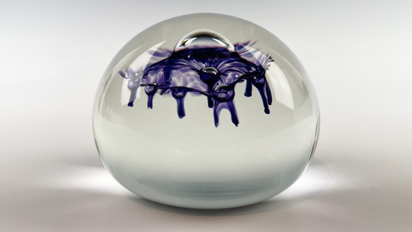 A clear air-trap paperweight with a large blue ink-like bubble at the top, is a possible creation of the air-trap paperweight make-your-own experience.