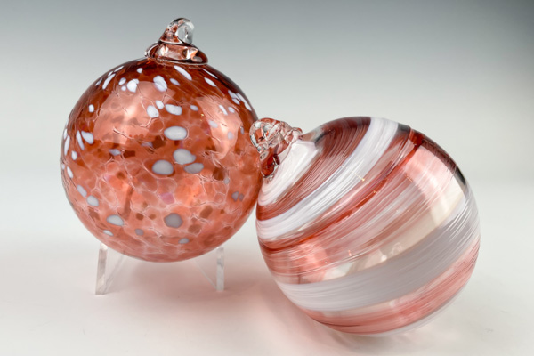 Two pink & clear ornaments are side by side. The one on the left has specks of color and has a crackle effect over its surface. The right has a swirl pattern.