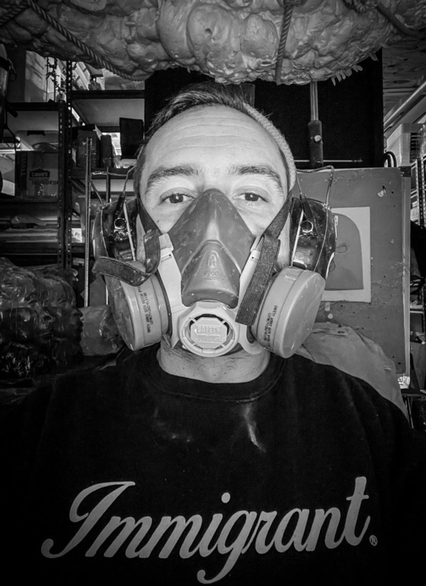 This image is a headshot of 2023 creative glass fellow Esteban Salazar, who is wearing a breathing mask used for working with chemicals and a black shirt.