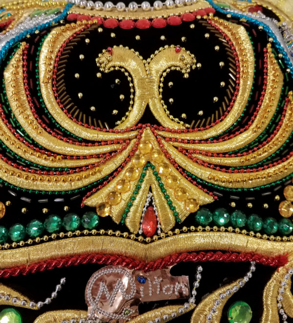 A close-up of the detail on a costume from the Folklife Center exhibit The Good, the Evil, and the Funny: Ritual & Mask Dance of Latin America. The costume has a black base color with gold, red, and green details on it.