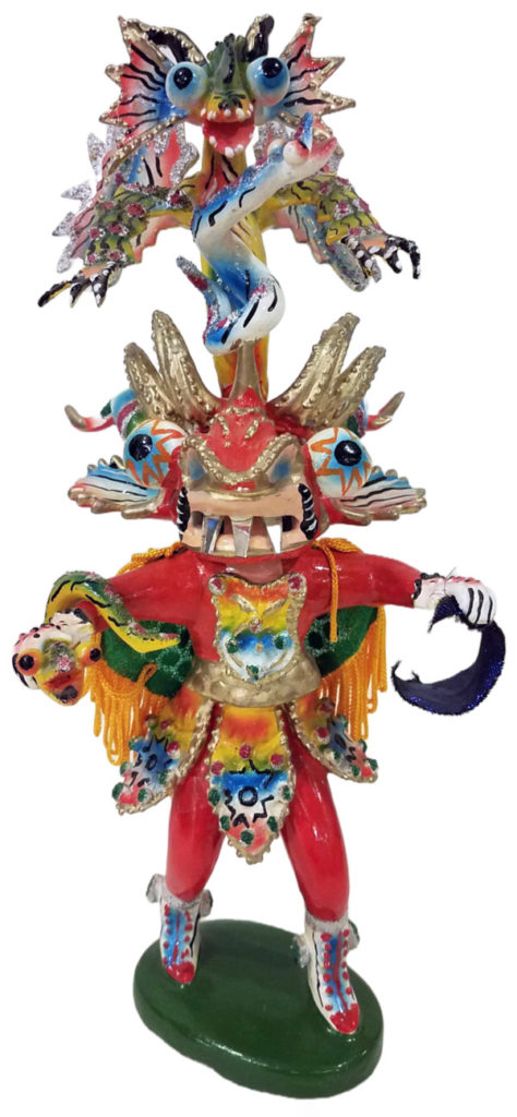 A close-up of a sculpture from the Folklife Center exhibit The Good, the Evil, and the Funny: Ritual & Mask Dance of Latin America. The sculpture appears to be a warrior wearing red and blue armor and a green & blue dragon coming from the top. The sculpture is of a traditional costume.