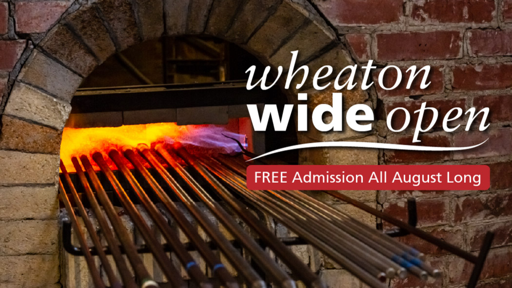 The image shows a banner that reads "Wheaton Wide Open" in large white text in the upper right corner. A long horizontal red rectangle sits underneath with white text inside that reads "FREE Admission All August Long". A burning brick heating chamber is pictured behind the text with seventeen glass blowing poles sticking outside of the opening.