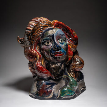 Image of artwork by Miranda Blas. The sculpture is a bust of a woman with wavy shoulder length hair. The eyes of sculpture are white with a dark pupil and the head is angled so that it is staring up into the distance. The lips are dark read and the skin is a marble pattern of different shades of black, purple, blue, red, and green. The hair is a mix of various shades of red, orange, brown, and yellow and has been carved so that that the strands of hair are detailed and textured. The entire sculpture sits in front of a white to black gradient background.