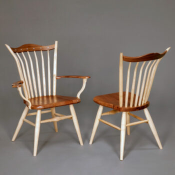 Image of two wooden chairs in front of a gray background. Each chair has a brown top rail, seat, and armrest. The backings, arm supports, and legs of the chair are white.