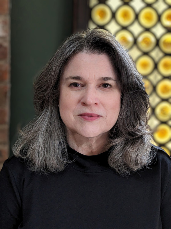 Headshot of Mary Mills. Mary is wearing a black shirt and has shoulder-length light and dark hair.