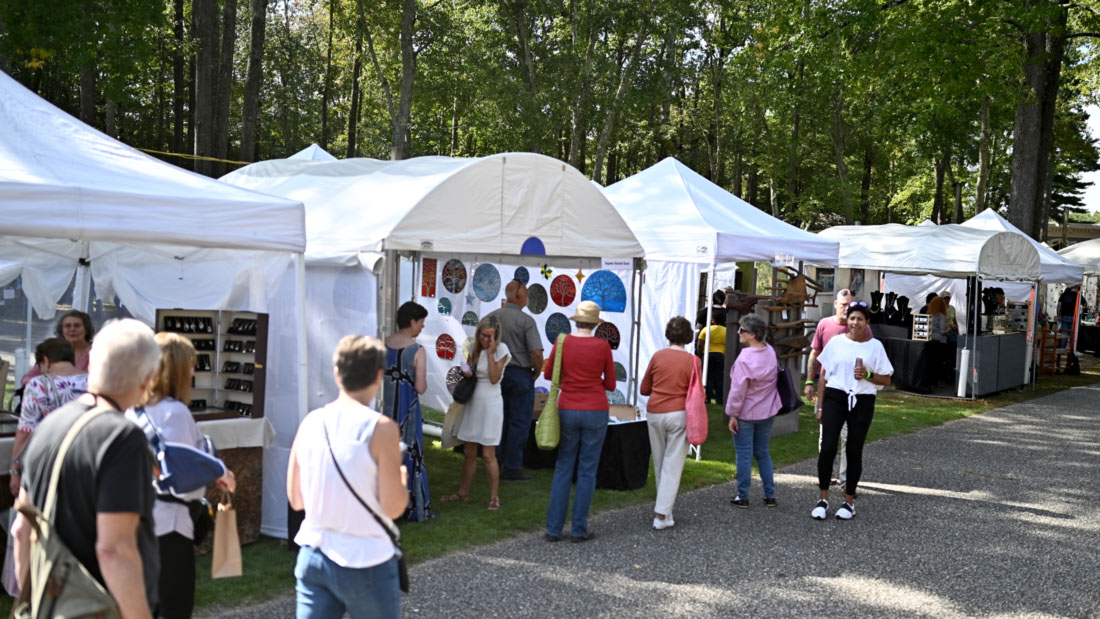 Image of a crowd of visitors shopping at vendors under white tents outside at an event at WheatonArts.