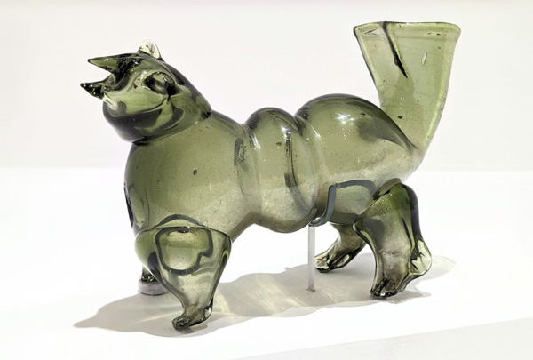Image of a Liquor Dog in front and on top of a white backdrop. The piece is made up of green-tinted glass and is shaped to represent a dog and hold liquor.