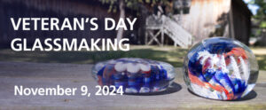 Image of the banner for the Veterans Day Glassmaking program. The background of the banner is an image of two red, white, and blue swirl glass paperweights resting outside on a wooden picnic table in front of the WheatonArts Glass Studio. The paperweight on the left is disc-shaped, while the paperweight on the right is orb-shaped. They both are on the right side of the banner. The left side of the banner has a dark transparent shadow with white lettering on top that reads "Veteran's Day Glassmaking" with more white text underneath that reads "November 9, 2024".
