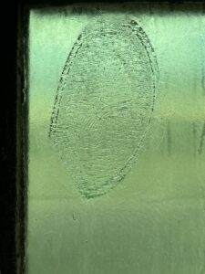 Image of a panel of green glass. There is a large e oval-shaped imprint on the glass. The glass is textured where the imprint is.